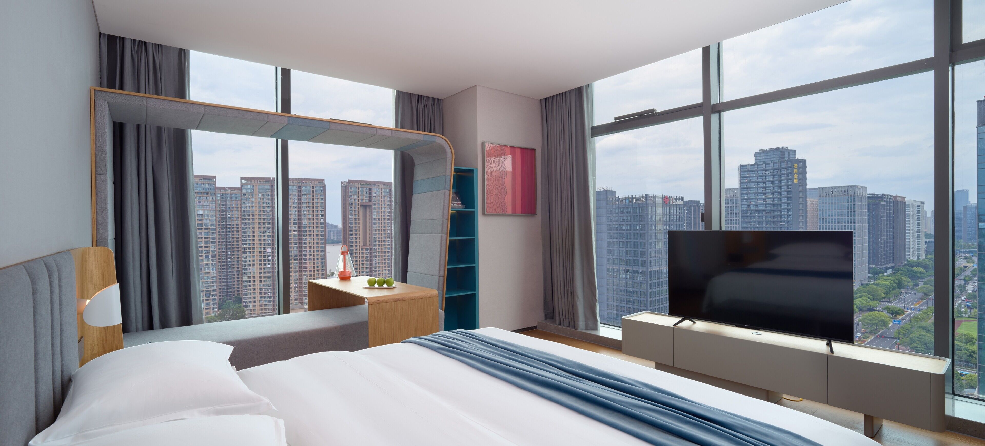Una habitación de hotel moderna con una cama grande, un televisor, un escritorio con lámpara y vistas a la ciudad.