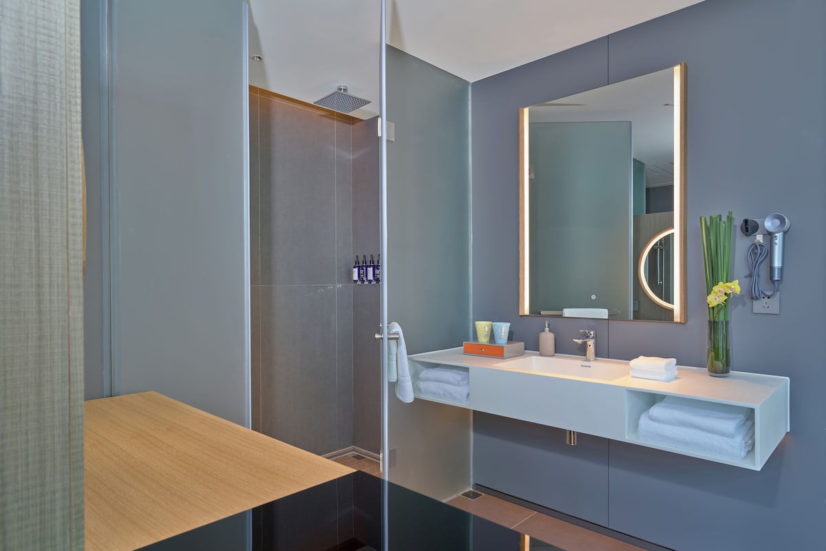 A modern bathroom with a glass shower enclosure, a white vanity with a mirror, and a vase with flowers.