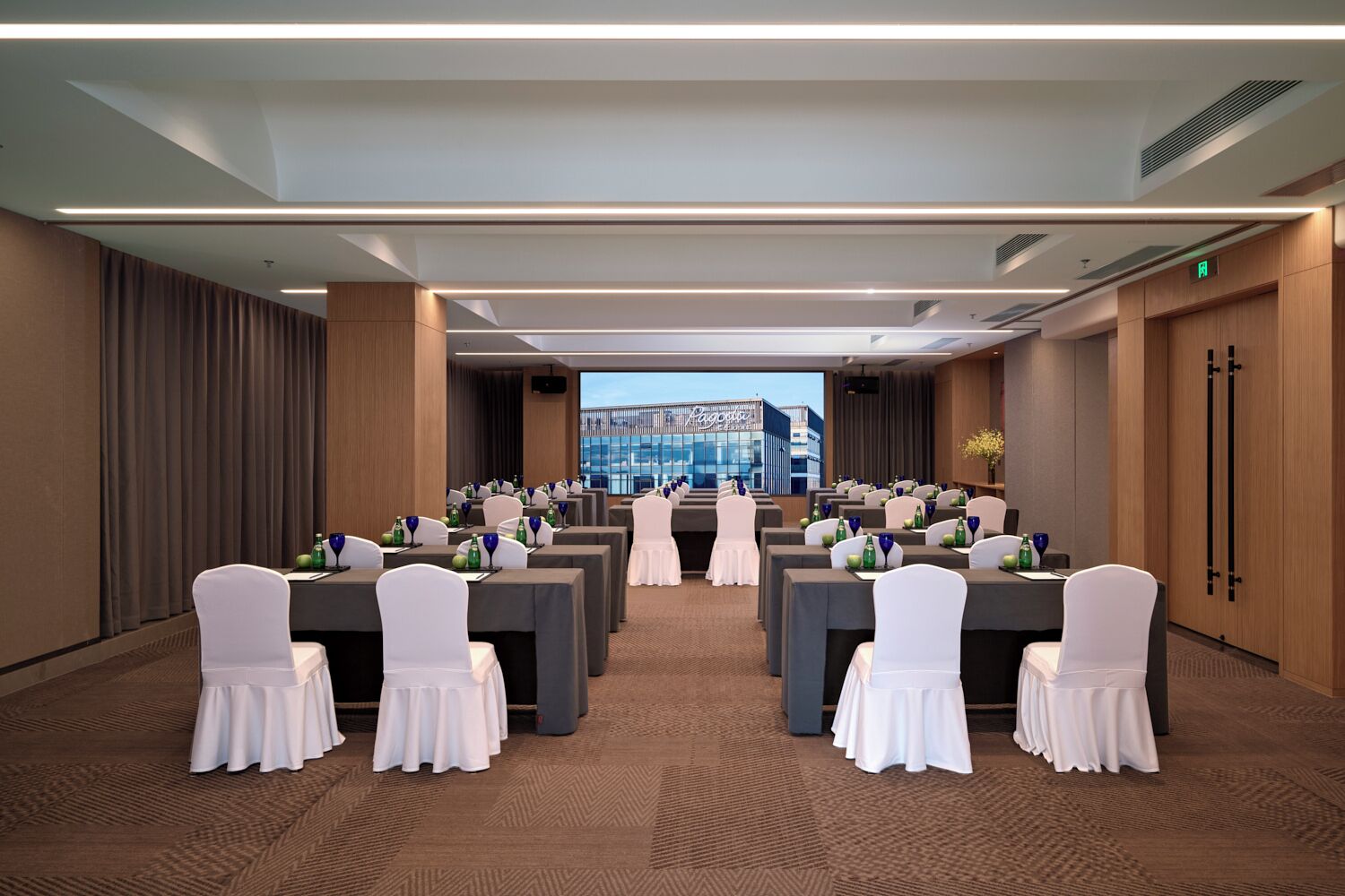 A conference room with tables set for a meeting, a view of a building, and a door with a sign.