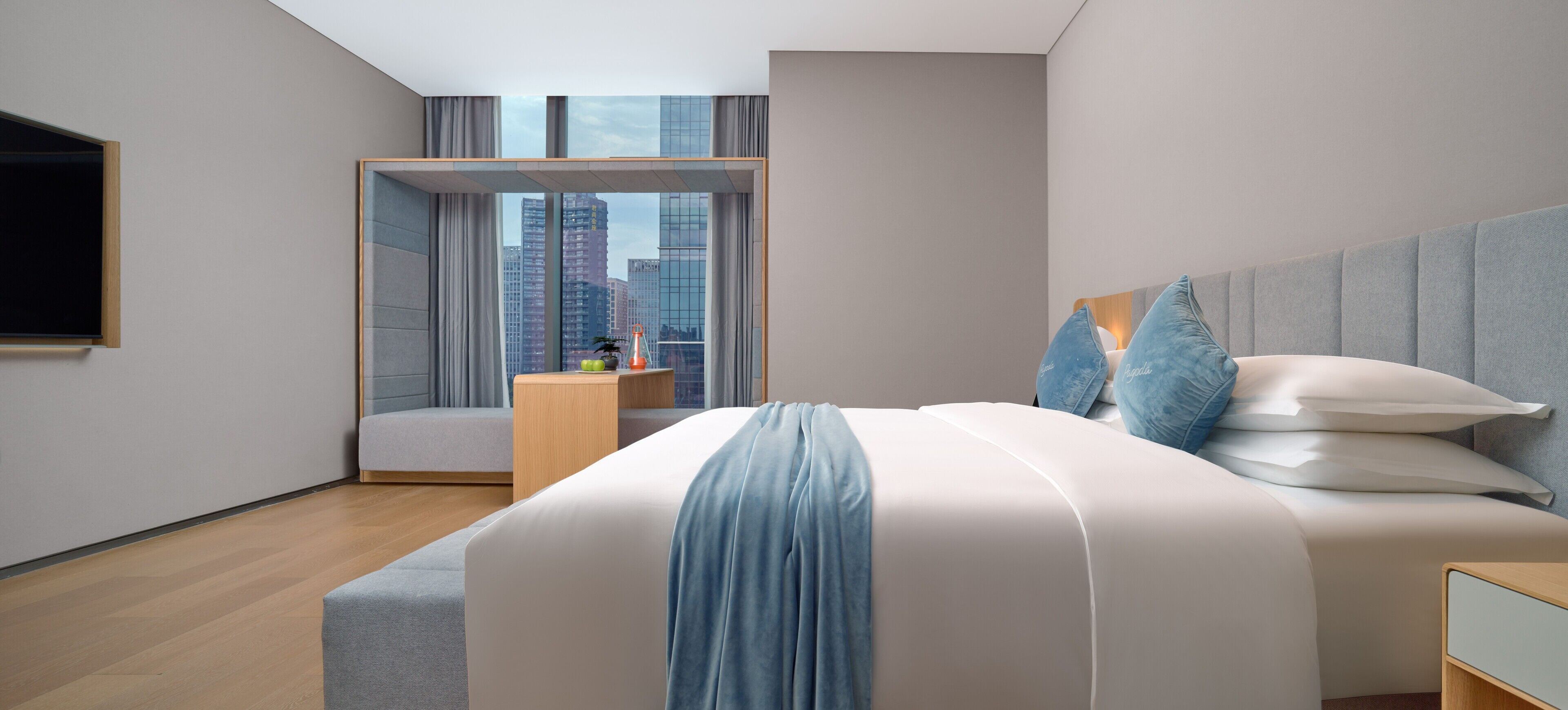 Quarto de hotel moderno com uma cama grande, mesa de cabeceira, televisão e vista para a cidade pela janela.