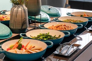 Una mesa de buffet con varios platos en cuencos azules y blancos, un florero con follaje y una olla sobre un soporte.