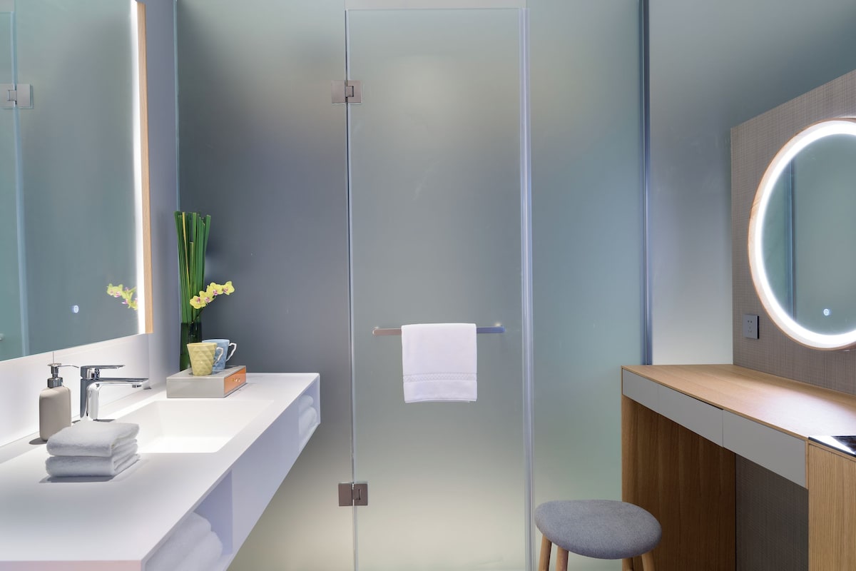A modern bathroom with a white vanity, a large mirror, a round mirror, and a hair dryer on the wall.