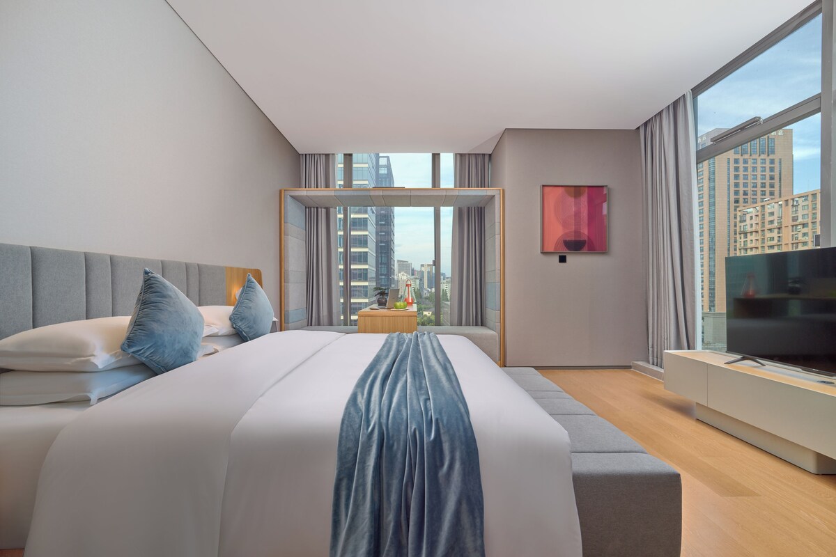 A modern hotel room with a large bed, a TV, and a city view.