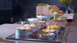 Un bufé con diversos alimentos, como mazorcas de maíz y albóndigas, dispuestos en una larga mesa.