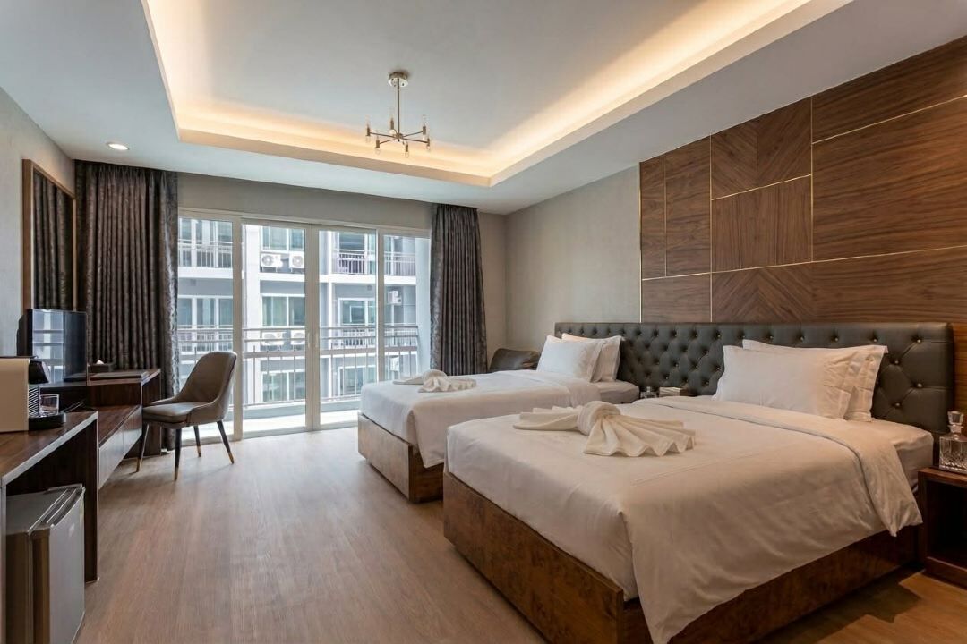 A hotel room with two beds, a desk, a chair, and a view of the city.