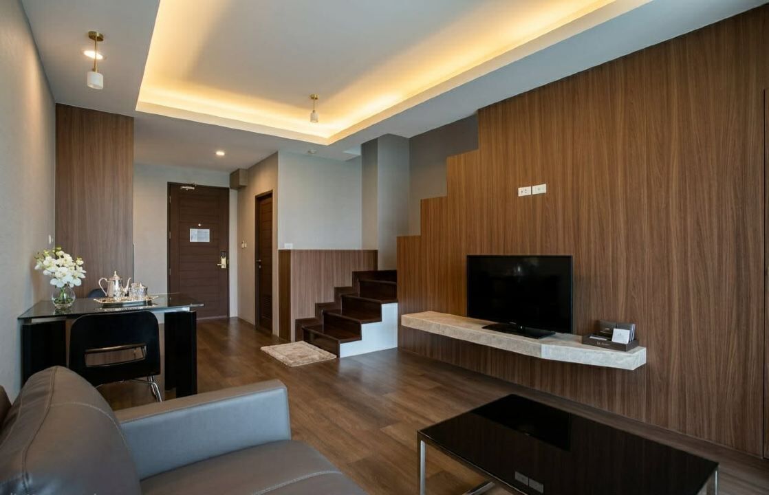 Una sala de estar moderna con un televisor de pantalla plana, un sofá, una mesa de centro y una escalera que sube a otro nivel.