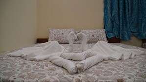 A bed with a floral-patterned bedspread and two towels arranged in the shape of swans. - Sonajhuri Bagan Bari (Bolpur)