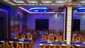 A restaurant with wooden chairs and tables, a mural on the wall, and modern lighting fixtures. - Sonajhuri Bagan Bari (Bolpur)