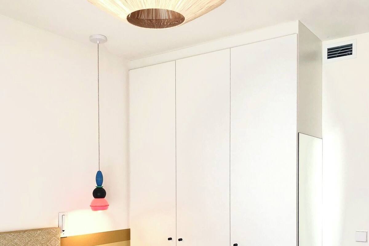 A hotel room with a bed, a bedside table, a wardrobe, and a hanging light fixture.