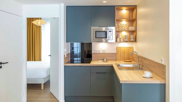Cocina compacta con microondas, lavabo y estantes de madera.