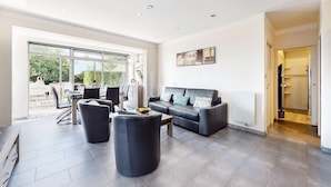A spacious living area with a black leather sofa, two black ottomans, and a dining table with chairs. A large sliding glass door leads to an outdoor patio. - Awesome home in Saint-Pierre-d'Oléron with WiFi (Saint-Pierre-d'Oléron)