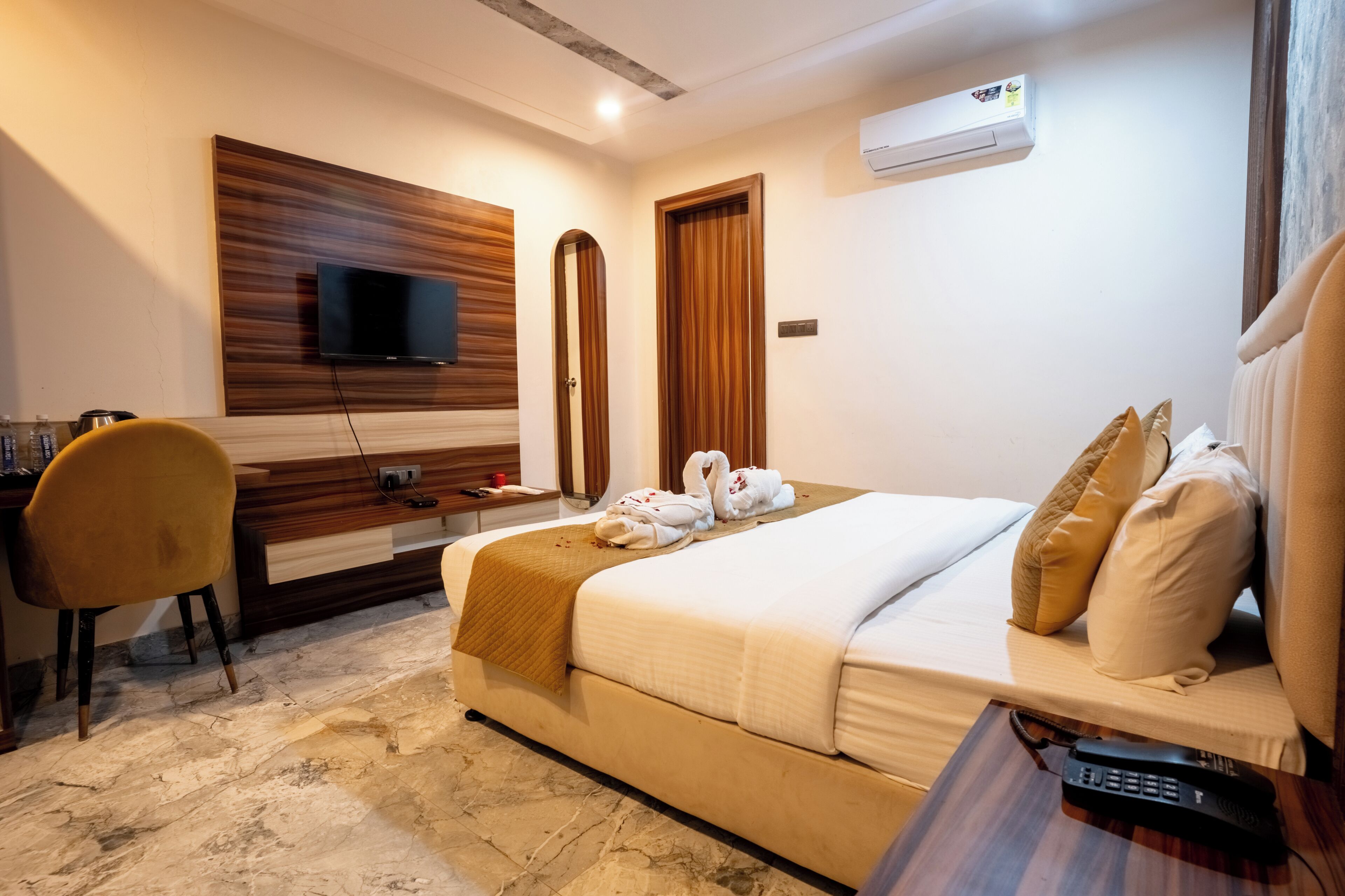 A hotel room with a bed, a desk, a chair, a TV, and an air conditioning unit.