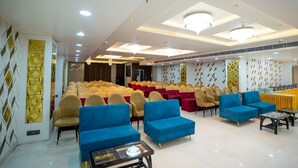 Une salle de conférence avec des rangées de chaises, une scène et des canapés bleus et beiges.