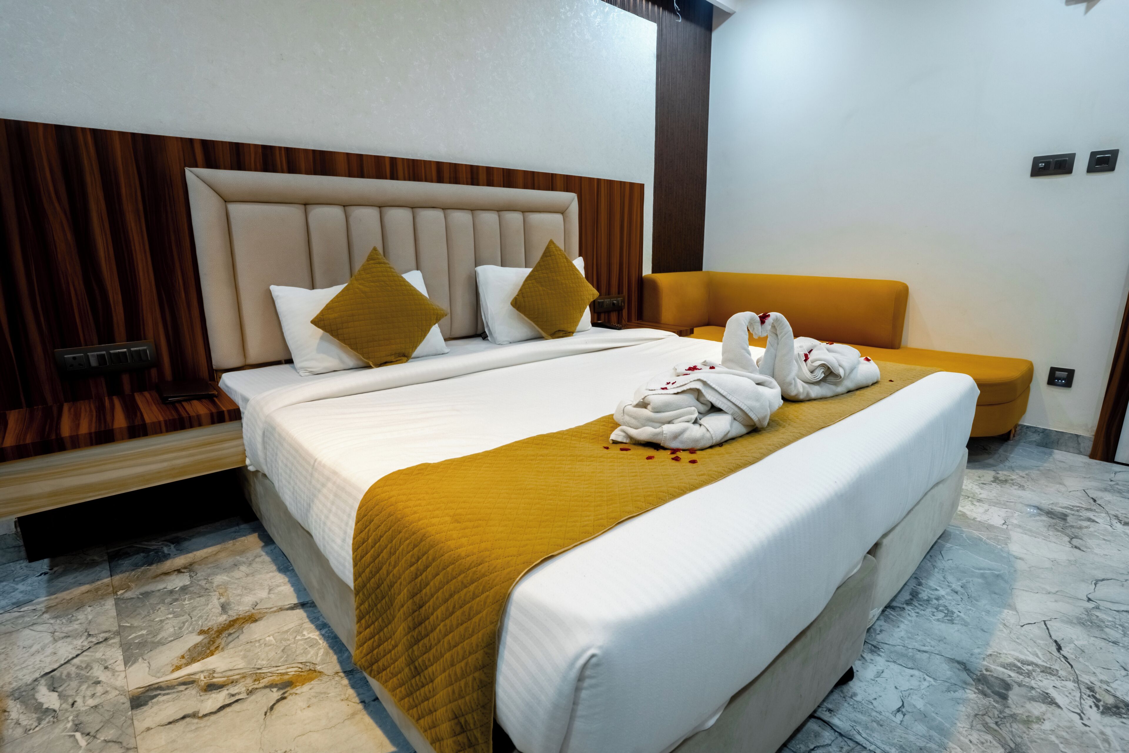 A hotel room with a large bed, a wooden headboard, a yellow armchair, and a marble floor.