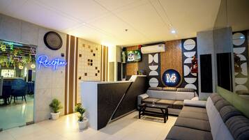 A reception area with a neon sign, a clock, a TV, a reception desk, sofas, and potted plants.
