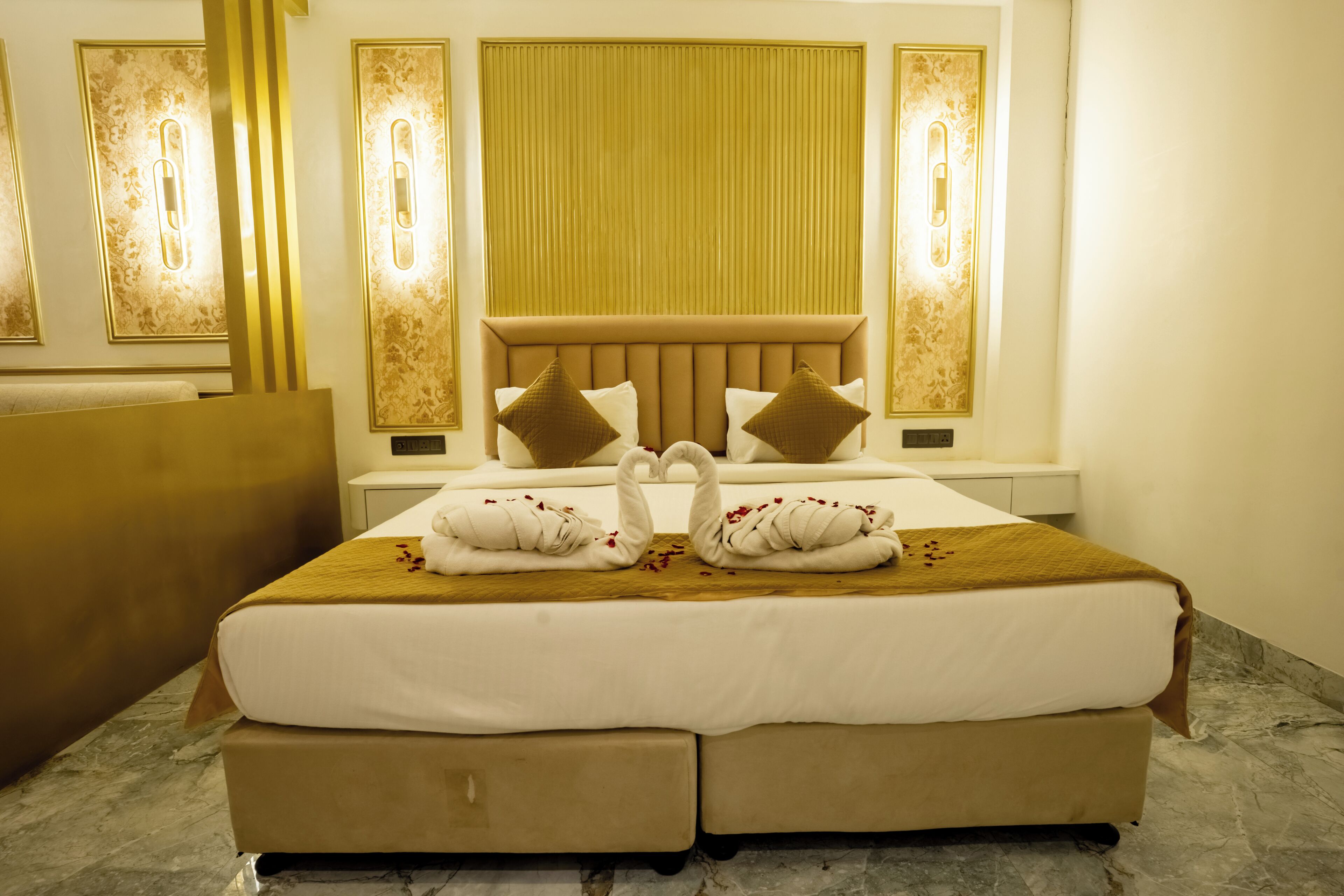 A hotel room with a large bed, a headboard, bedside tables, and wall-mounted light fixtures.