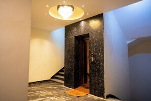 A modern interior with a marble floor, a wooden door, and a chandelier. - The Manor by Tulip Hospitality (Varanasi)