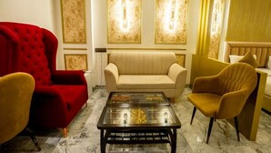 Un salon avec un canapé rouge, un canapé beige et des fauteuils jaunes. Une table basse en verre se trouve au centre de la pièce.