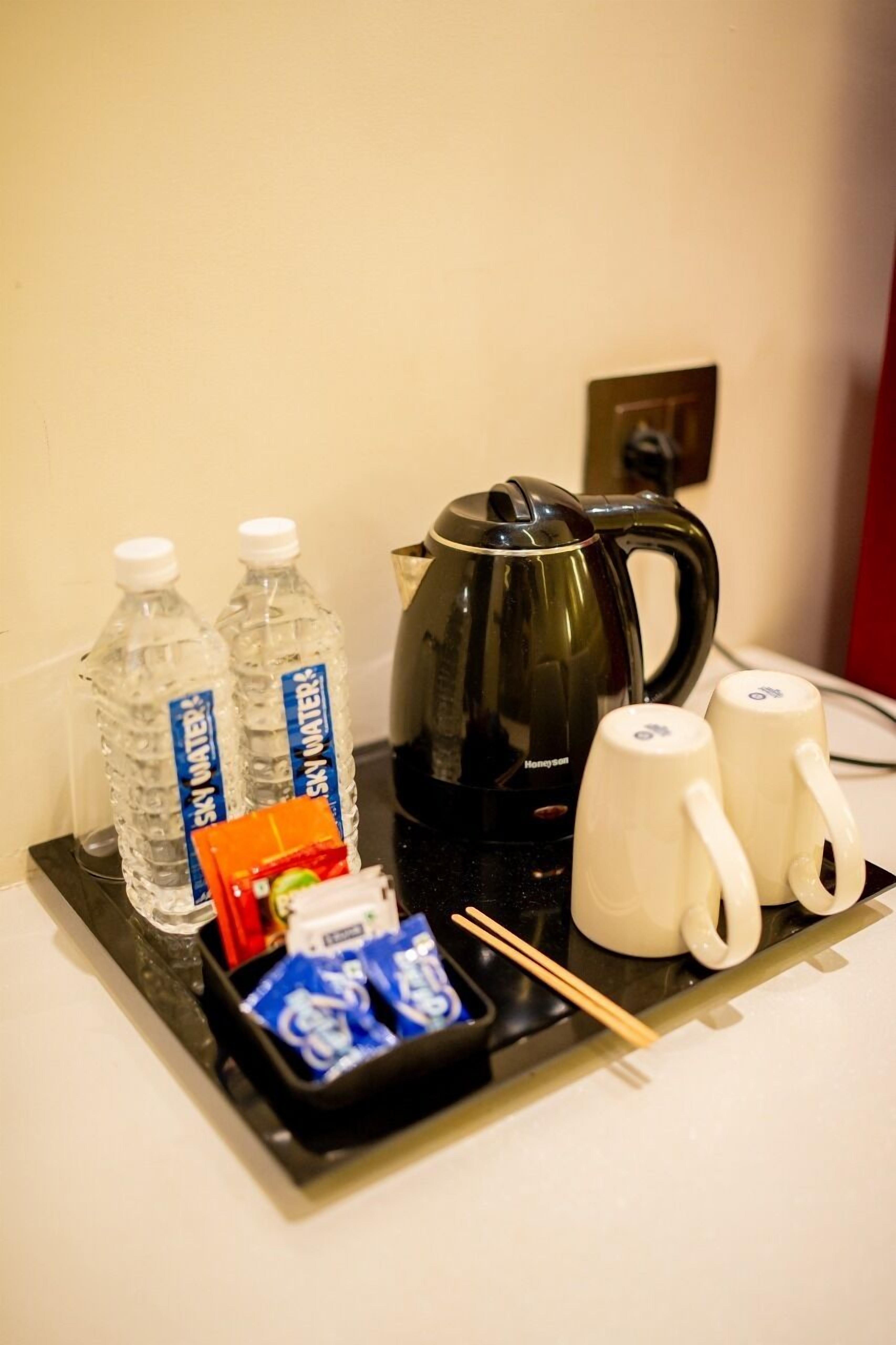 Un plateau avec deux bouteilles d’eau, une bouilloire électrique noire, deux tasses blanches et quelques en-cas emballés.