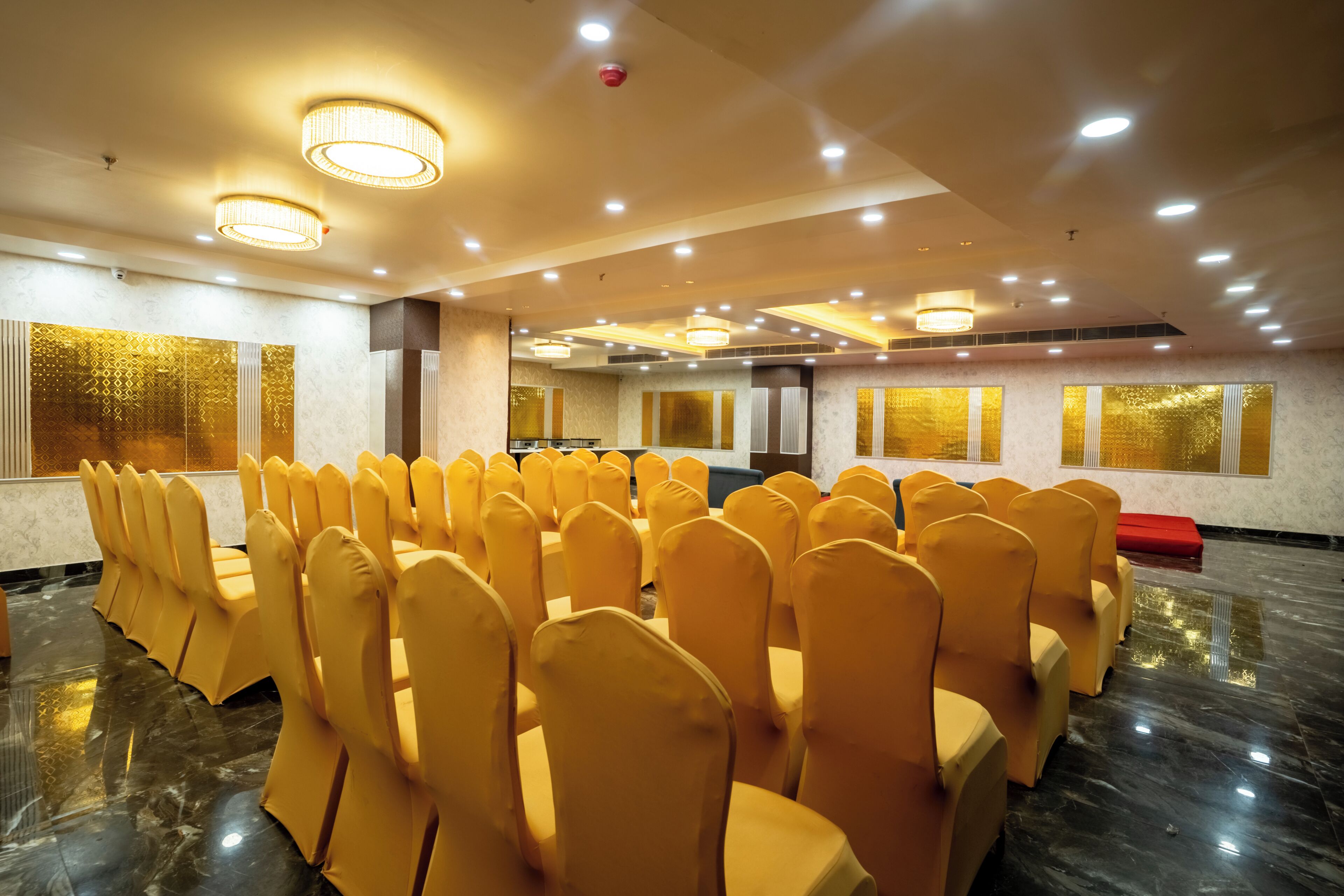 A conference room with rows of chairs, a stage, and ceiling lights.