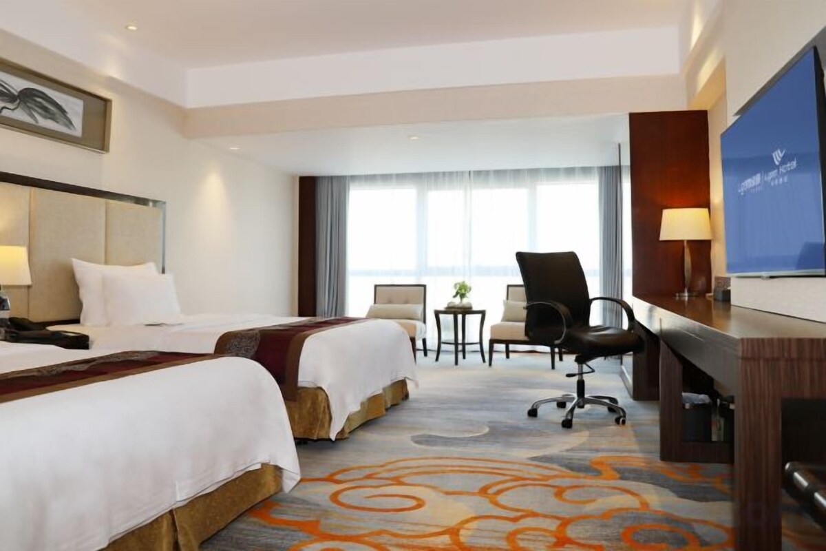 A hotel room with two beds, a desk, a chair, a TV, and a small table with a plant.