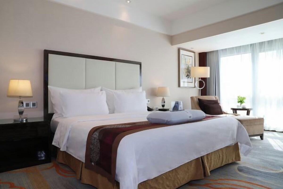 A hotel room with a large bed, two bedside tables with lamps, a chair, and a view of the outdoors.