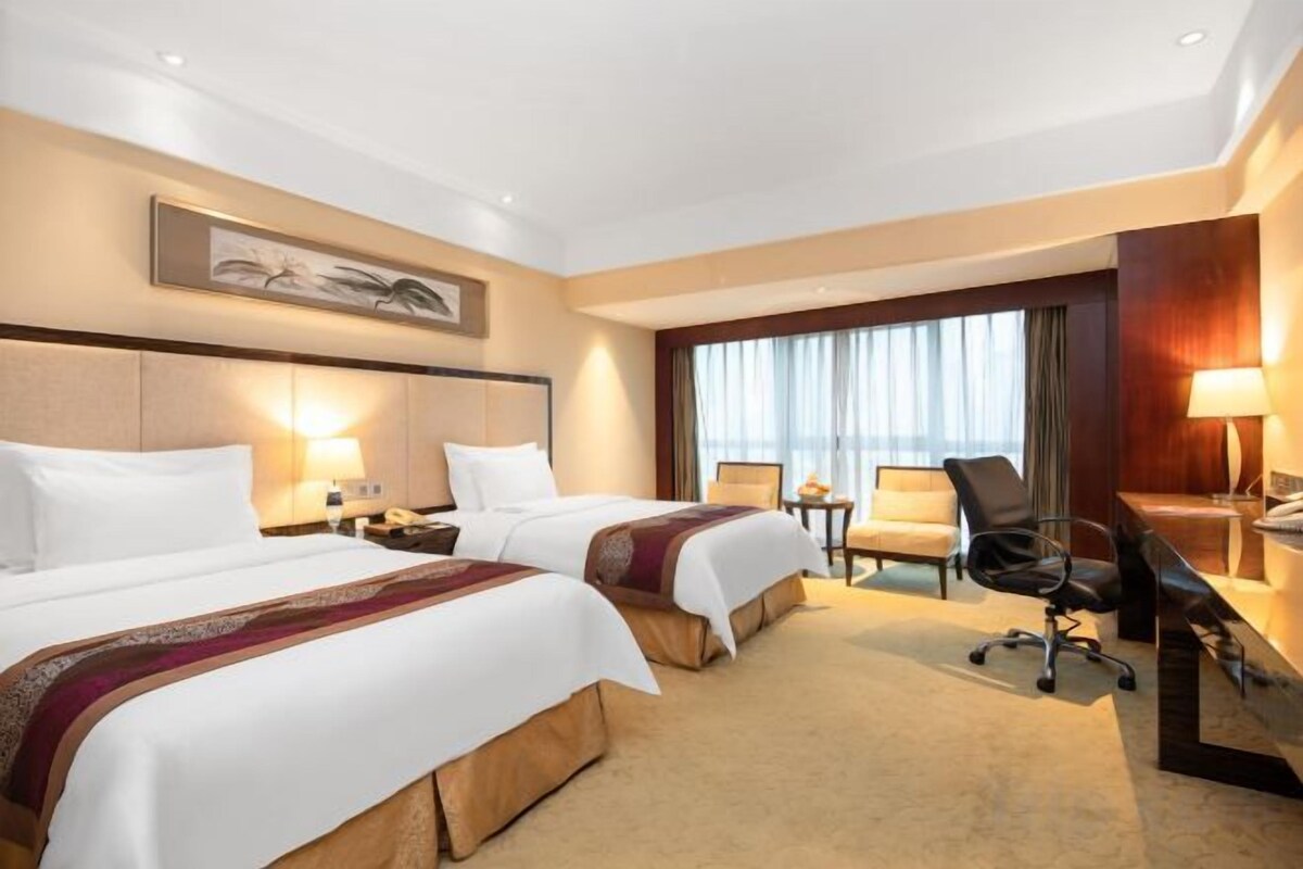 A hotel room with two beds, a desk, a chair, and a large window with curtains.
