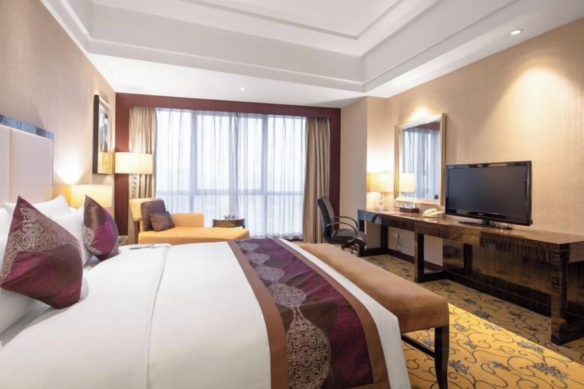 A hotel room with a large bed, a desk, a television, and a window with curtains.