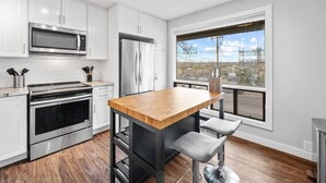 A modern kitchen with white cabinets, stainless steel appliances, a wooden island, and a large window with a city view.