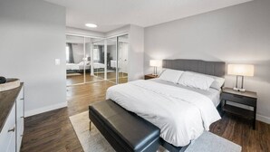 A modern bedroom with a large bed, bedside tables, a bench, and a walk-in closet with mirrors.