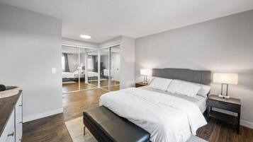 Une chambre moderne avec un grand lit, des tables de chevet, un banc et un dressing avec des miroirs.