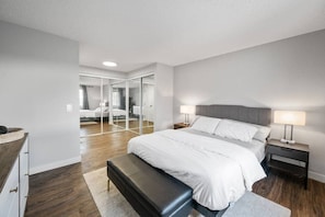 Quarto moderno com uma cama grande, mesas de cabeceira, um banquinho e um closet espaçoso com espelhos.