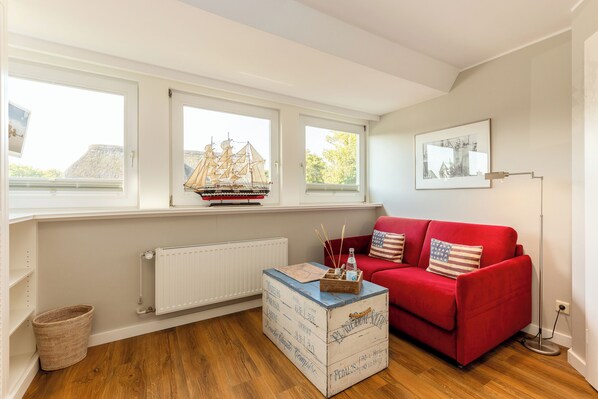Una habitación con un sofá rojo, una mesa de centro de madera y un modelo de barco en el alféizar de una ventana.