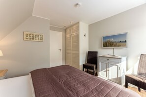 Un dormitorio con cama, escritorio con silla, televisor y armario.