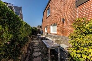 Una casa de ladrillo con patio jardín, un banco de madera y una pequeña mesa.