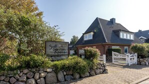 A house with a stone wall, a wooden sign, and a white gate. - Sylt Rooms 10 - Shelter Island - Westerland (Westerland)