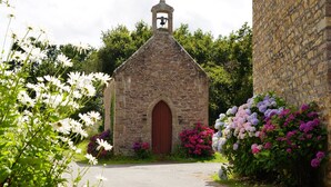 A small stone church with a bell tower, surrounded by lush greenery and vibrant flowers.