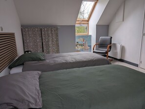 A bedroom with two beds, a chair, a radiator, and a skylight.