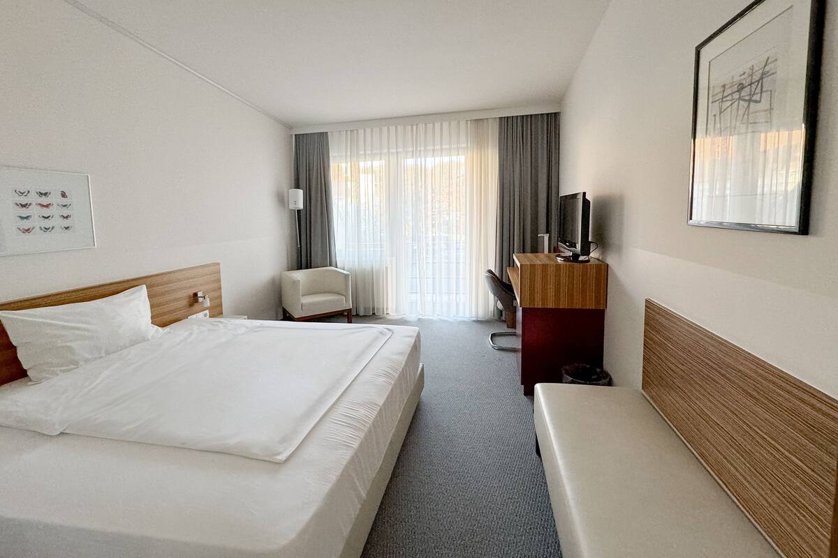 A hotel room with a large bed, a desk, a chair, a television, and a framed picture on the wall.