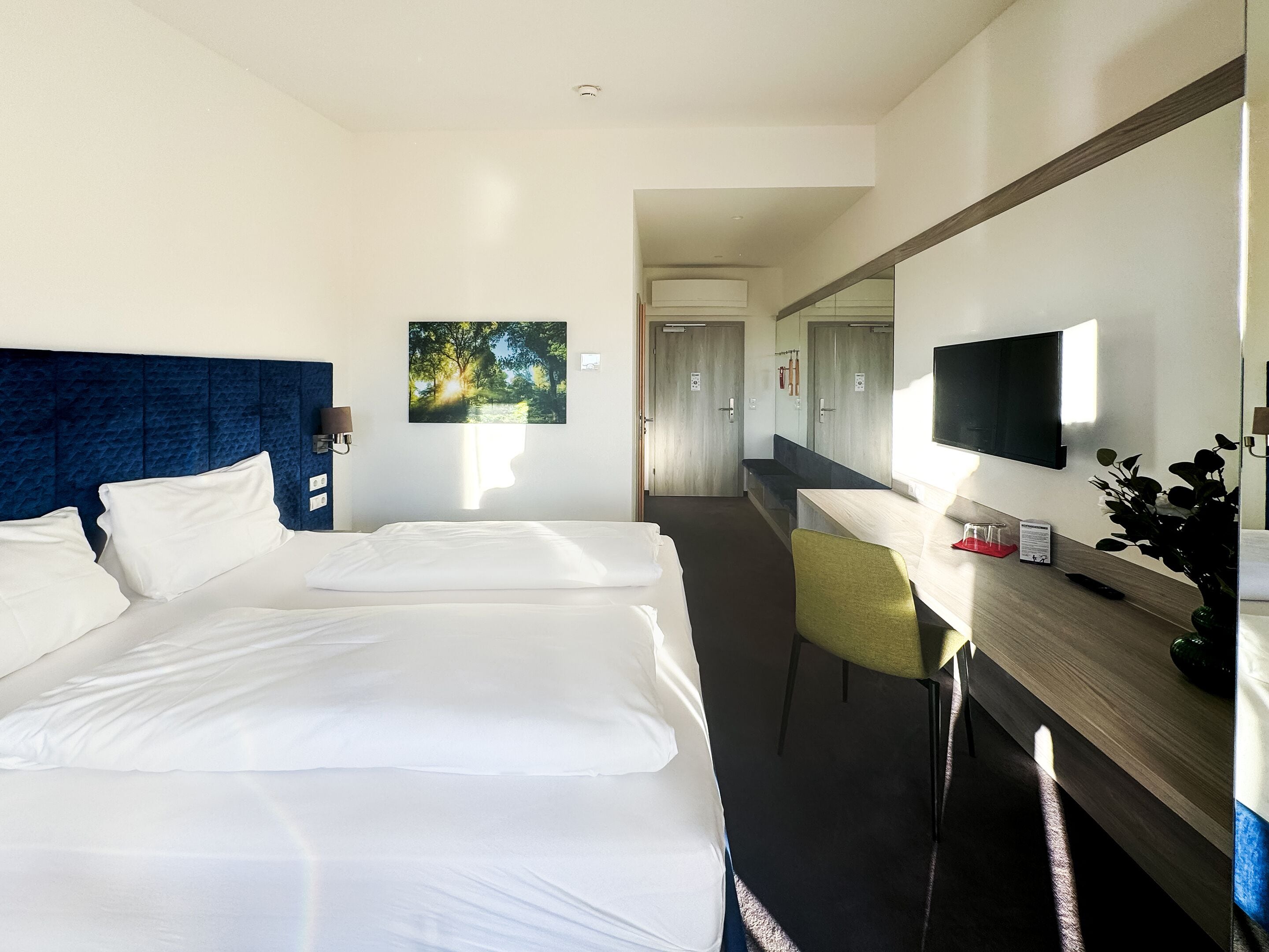 A hotel room with two beds, a desk, a chair, a TV, and a painting on the wall.