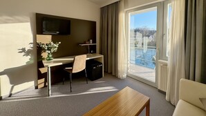 Ein Hotelzimmer mit Schreibtisch, Stuhl, Fernseher und Balkonblick.