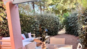 An outdoor patio with a wooden table set for dining, surrounded by white chairs and a cushioned seating area. - Mini Villa U Campa Be - 5 people 250 m from the beach San Cyprianu Corsica (lecci)