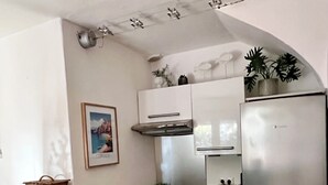 A compact kitchen with a built-in stove, oven, and a stainless steel refrigerator. There is a small island with a fruit bowl and a basket. - Mini Villa U Campa Be - 5 people 250 m from the beach San Cyprianu Corsica (lecci)