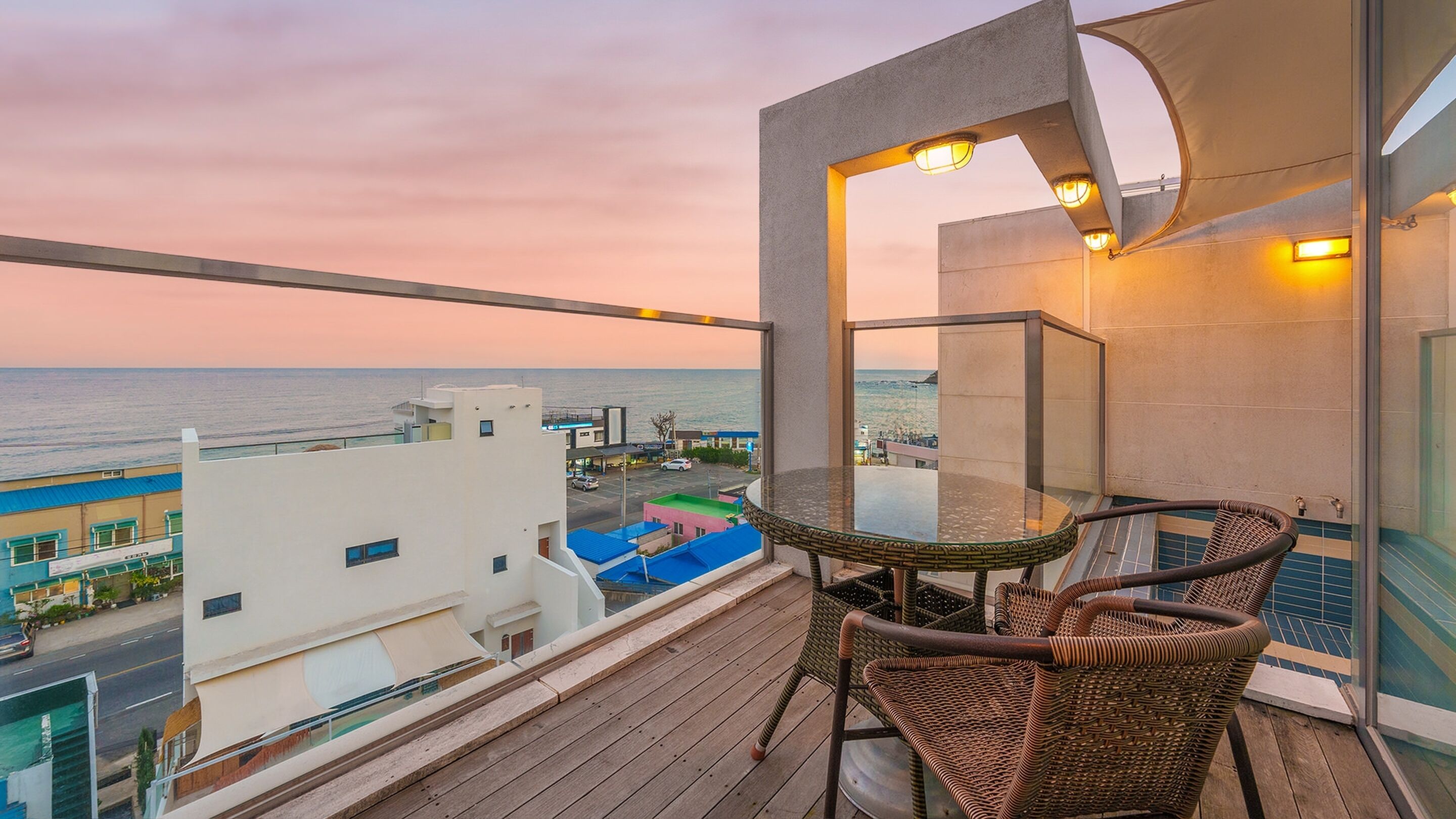 A balcony with a table and chairs, overlooking a cityscape and the sea.