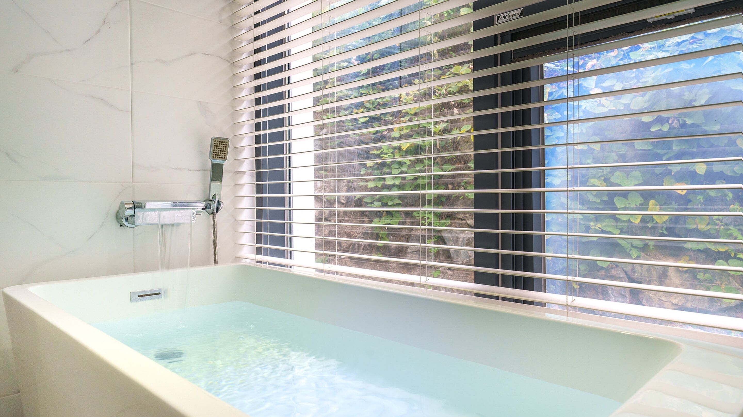 A modern bathroom with a freestanding bathtub, a showerhead, and a window with blinds.