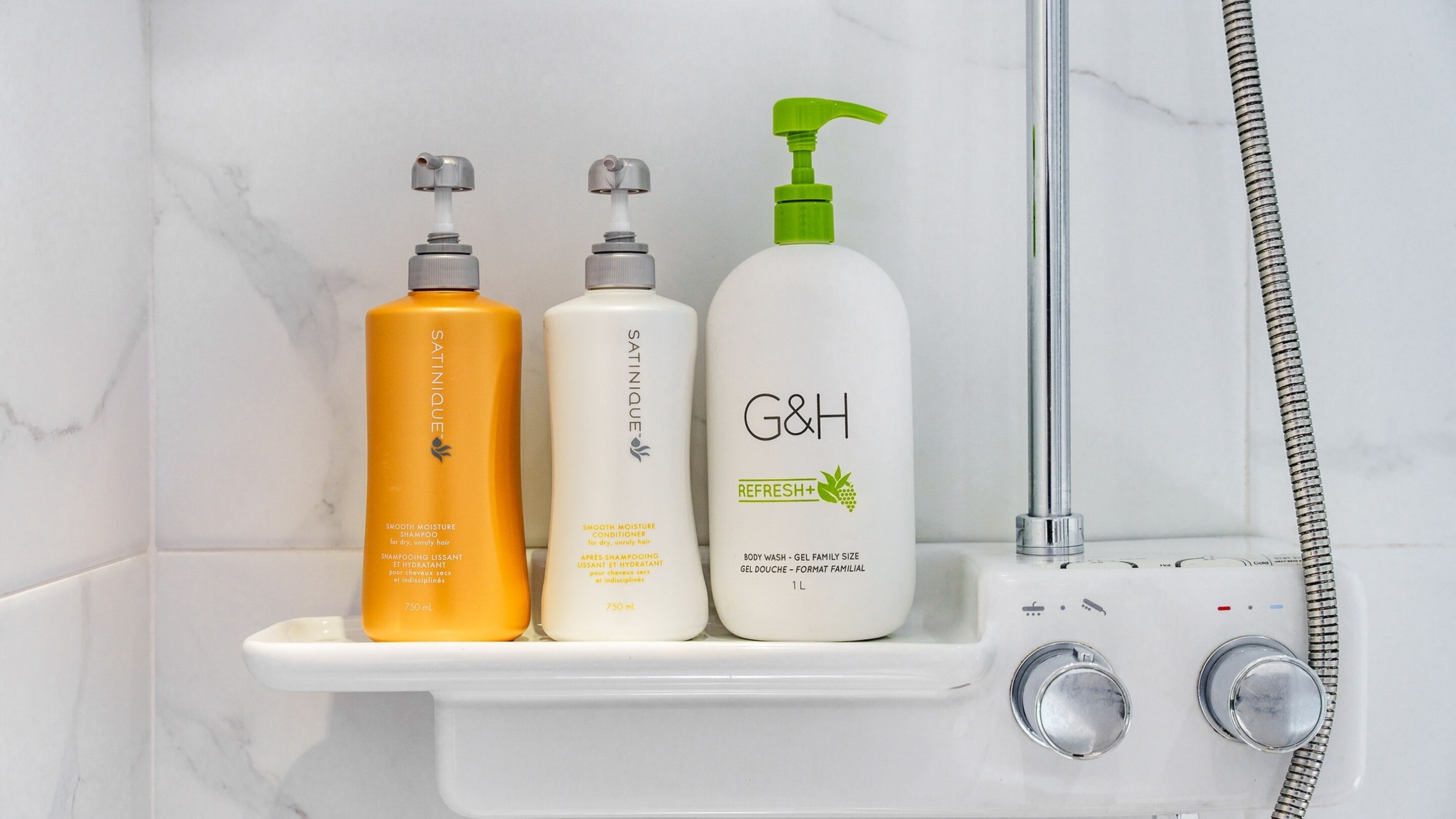 A bathroom shelf with three bottles of hair care products and a showerhead.