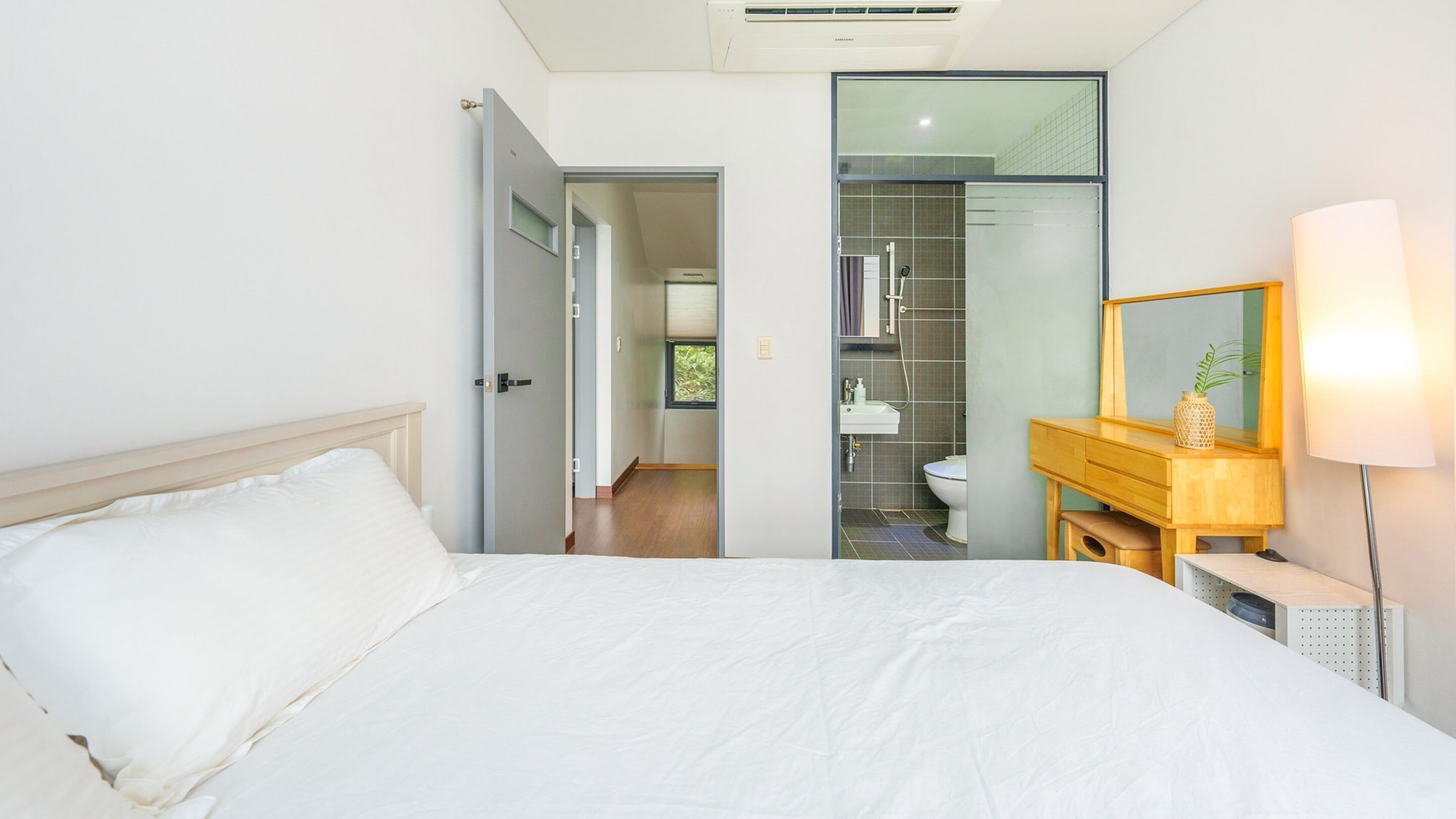 A bedroom with a bed, a wooden nightstand, a mirror, and a bathroom visible through an open door.