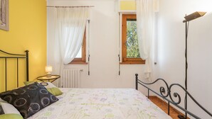 Una camera da letto con un letto, un comodino, una lampada, una finestra con tende e un termosifone.