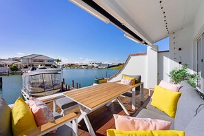 A balcony with a wooden table and chairs, a sofa with cushions, and a view of a marina with boats and houses. - On the Canal in Halls Head (Halls Head)
