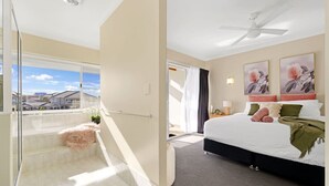 A hotel room with a balcony, a bed with pillows and a blanket, a ceiling fan, and artwork on the wall.